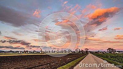 Beautiful landscape with road, fields and blue sky covered partially with fluffy colorful clouds in the background Stock Photo