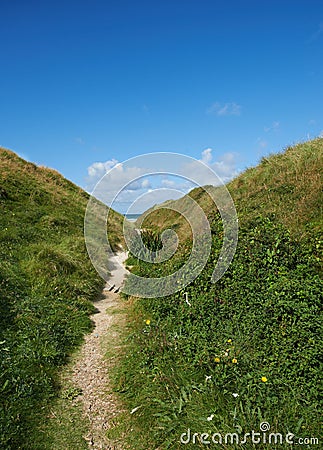 Beautiful landscape with a secret path between grassy hills to a hideaway, hidden beach or secluded area with a blue sky Stock Photo
