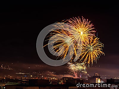 Beautiful large firework splashes high in the night sky over a city. Townspeople launching fireworks at New Year midnight. Stock Photo