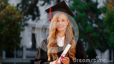 Beautiful with a large smile lady graduate posing in front of the camera while holding her diploma in the college garden Stock Photo