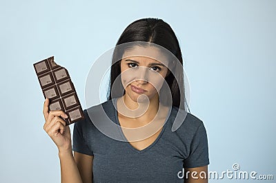 Beautiful latin woman with chocolate bar feeling guilty after biting on blue background in sugar and sweet abuse Stock Photo