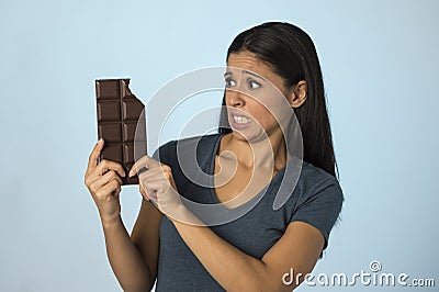 Beautiful latin woman with chocolate bar feeling guilty after biting on blue background in sugar and sweet abuse Stock Photo