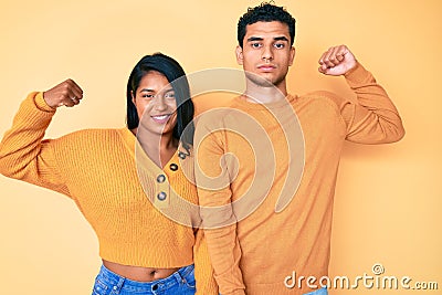 Beautiful latin young couple wearing casual clothes together strong person showing arm muscle, confident and proud of power Stock Photo