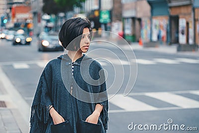 Beautiful Latin young woman in grey stylish poncho with fringe in urban street. Fashion and street style. Pretty hispanic brunette Stock Photo