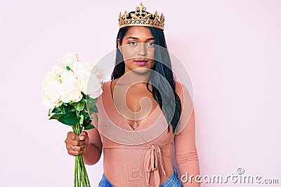 Beautiful latin young woman with long hair wearing princess crown and holding flowers thinking attitude and sober expression Stock Photo