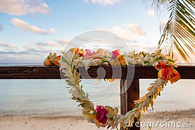 A beautiful lei of flowers rests on a the railing of a wooden deck overlooking a lagoon in French Polynesia in the South Pacific Stock Photo