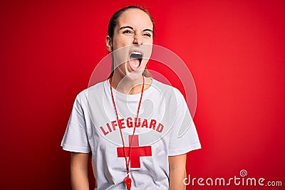 Beautiful lifeguard woman wearing t-shirt with red cross using whistle over isolated background angry and mad screaming frustrated Editorial Stock Photo