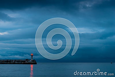 Beautiful lighthouse on the seashore at dusk, rainy clouds over Stock Photo