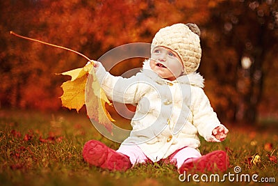 Beautiful little baby girl sitting with a big leaf at autumn park Stock Photo