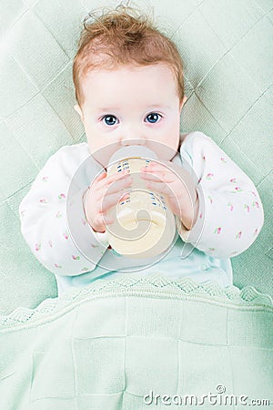 Beautiful little baby with a milk bottle under knitted blanket Stock Photo