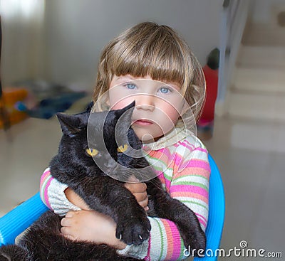 A beautiful little girl with blue eyes is holding a black cat. Friendship with pets. Stock Photo
