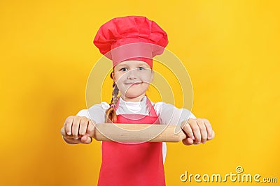 Beautiful little girl chef on a yellow background. The child holds in his hands a wooden rolling pin Stock Photo