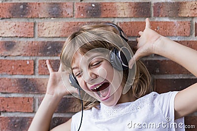 beautiful little girl with headphones at home listening to music and singing, technology and music concept. Brick background. Stock Photo