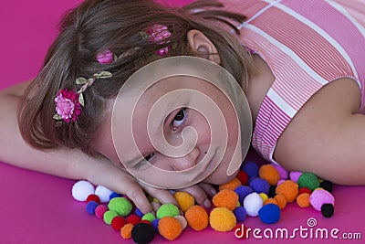 Beautiful little girl lying down on colorful pom poms Stock Photo