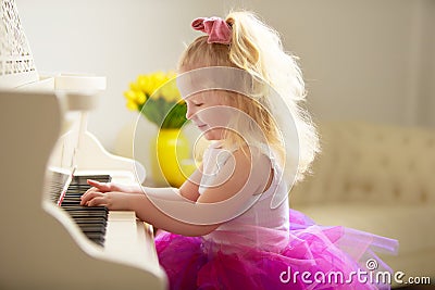 Beautiful little girl is playing on a white grand piano. Stock Photo