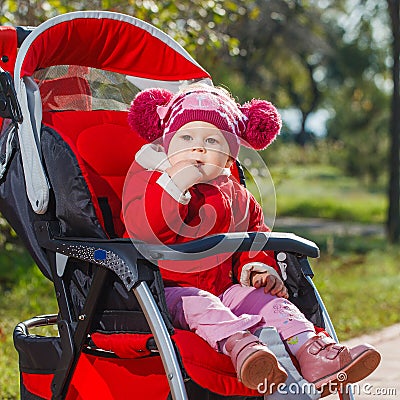 Beautiful little girl in a red jacket on the pram in park Stock Photo
