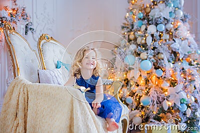 Beautiful little girl sitting on a sofa near christmas tree. Light interior. Smiling. Christmas. New year. Presents. Stock Photo