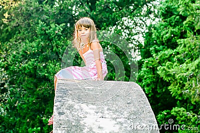 Beautiful little girl sitting on the stone structure Stock Photo