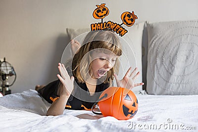 beautiful little girl smiling and wearing halloween costume on bed. playing with pumpkins. Home, indoors, lifestyle Stock Photo