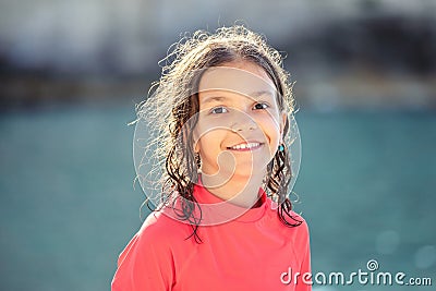 Beautiful little girl with wet hair smiling and looking at camera at beach during sunset, Outdoor portrait of happy child Stock Photo