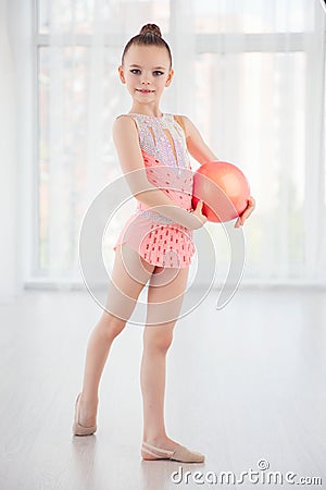 Beautiful little gymnast girl in pink sportswear dress, performing art gymnastics element with ball in fitness class Stock Photo