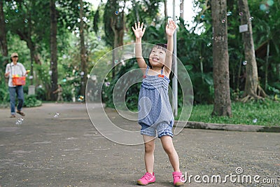 Beautiful little haired hair girl, has happy fun smiling face, pretty eyes, short hair, playing soap bubbles, dressed, Child Stock Photo