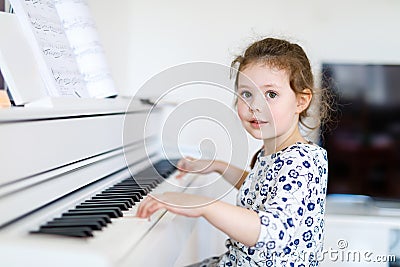 Beautiful little kid girl playing piano in living room or music school Stock Photo