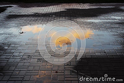 beautiful little pink cloud, illuminated by the setting sun, is reflected in a puddle in the square with paving tiles Stock Photo