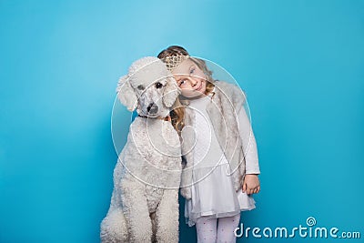 Beautiful little princess with dog. Friendship. Pets. Studio portrait over blue background Stock Photo