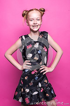 Beautiful little redhead girl in dress posing like model on pink background. Stock Photo