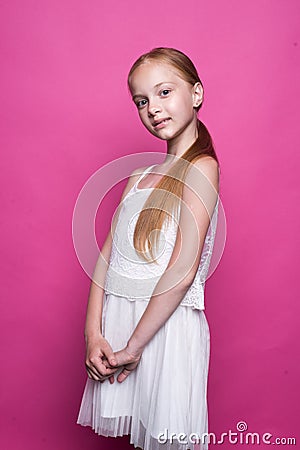 Beautiful little redhead girl in white dress posing like model on pink background. Stock Photo