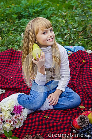 Beautiful little young baby in a pink hat with pear in hand. Beautiful child sitting on a red plaid. Stock Photo