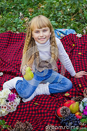 Beautiful little young baby in a pink hat with pear in hand. Beautiful child sitting on a red plaid. Stock Photo