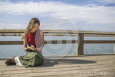 Beautiful long haired woman writing in journal near rural lake. Stock Photo