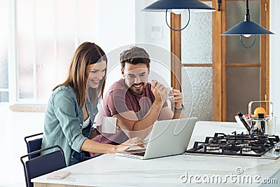 Beautiful lovely young couple using their laptop and having breakfast in the kitchen at home Stock Photo