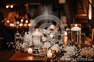 Beautiful luxury rustic wedding guest table decor - wooden tables with glass jars and candles, white roses and eucayptus leaves Stock Photo