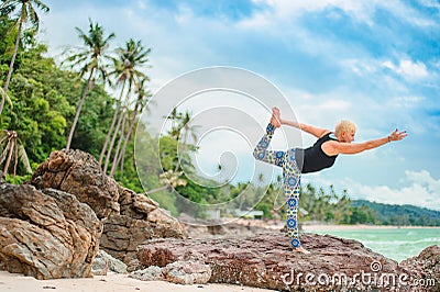 Beautiful mature aged woman doing yoga on a desert tropical beach Stock Photo