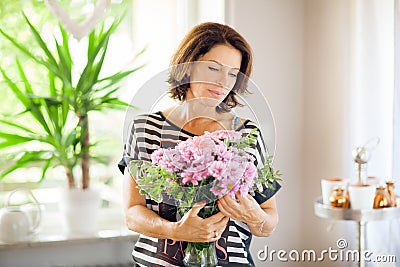 Beautiful middle age woman decorating home with flowers Stock Photo