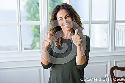 Beautiful middle age woman at home smiling cheerful doing ok symbil with thumbs up Stock Photo