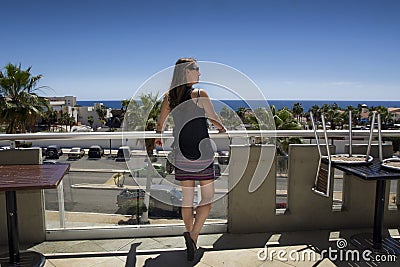 Beautiful Middle Aged Woman Watching Blue Ocean from Balcony with Deep Blue Sky. Long Brown Hair, Spaghetti Strap Top Stock Photo