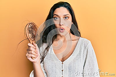 Beautiful middle eastern woman holding comb loosing hair scared and amazed with open mouth for surprise, disbelief face Stock Photo