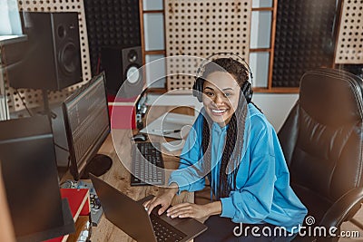 Beautiful woman sound engineer, radio presenter, smiles at camera while working on laptop in broadcasting studio Stock Photo