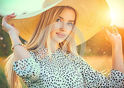 Beautiful model girl posing on a field, enjoying nature outdoors in wide brimmed straw hat. Beauty blonde young woman Stock Photo