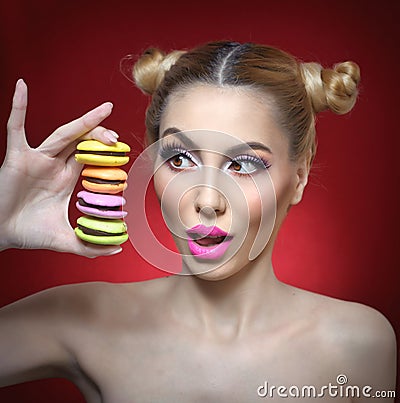 Beautiful model with makeup and creative hairstyle holding colorful macaroons, studio shoot on red background Stock Photo