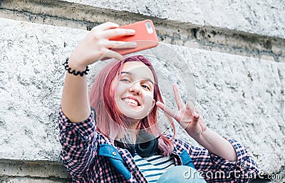 Beautiful modern smiling young female teenager with extraordinary hairstyle color taking selfie or video chatting via smartphone Stock Photo