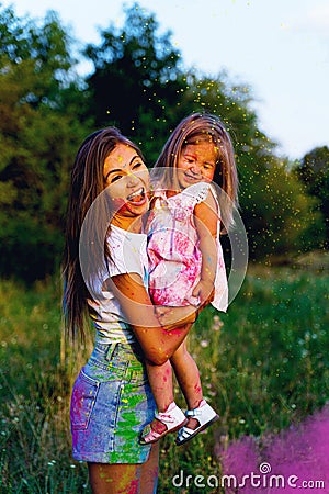 Beautiful mom and daughter play with Hol colors. multi-colored paint on clothes and face Stock Photo