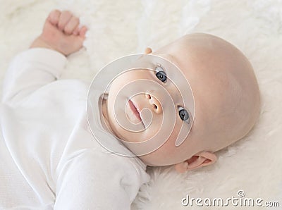 Beautiful 6 Month Baby Boy Dressed in White & Lying on Fluffy White Blanket Looking at Camera. Smiling & Happy Stock Photo