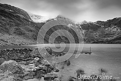 Beautiful moody Winter landscape image of Llyn Idwal and snowcapped Glyders Mountain Range in Snowdonia in black and white Stock Photo