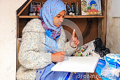 A beautiful Moroccan girl, a Muslim, street artist paints a picture with a brush in a small workshop Editorial Stock Photo