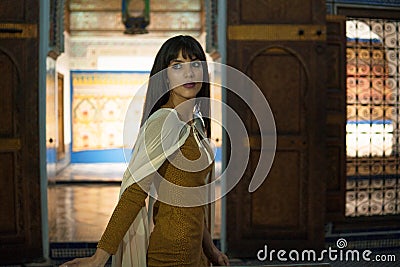 Beautiful Moroccan Girl in short golden dress and white mantle cloak in Rich interior of Picturesque Dar Si Said Riyad Editorial Stock Photo